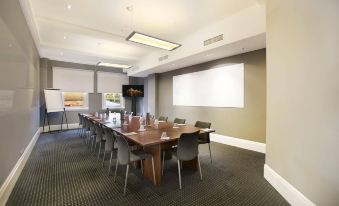 a conference room with a long table , chairs , and a projector screen set up for a meeting at Watsons Bay Boutique Hotel