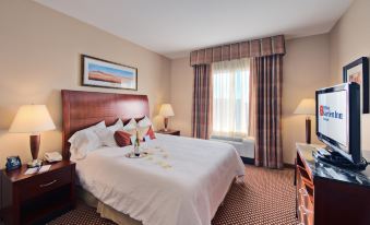 a large bed with white sheets and a wooden headboard is in a room with a window , lamps , and a painting at Hilton Garden Inn Laramie