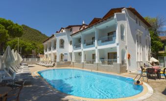 a large white hotel with a swimming pool , surrounded by mountains and clear blue skies at Arya Otel