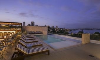 a rooftop pool with lounge chairs and a city skyline in the background at dusk at InterContinental Sydney Double Bay, an IHG Hotel
