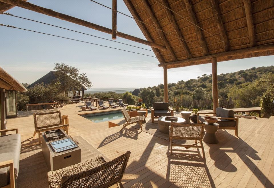 a spacious outdoor patio with a pool , surrounded by chairs and tables , providing a relaxing atmosphere at Bukela Game Lodge - Amakhala Game Reserve