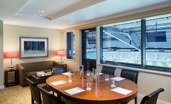 a large , round dining table with chairs is set up in a room with a couch and large windows at London Twickenham Stadium Hotel, a Member of Radisson Individuals