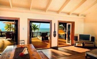 a wooden dining table with chairs , and a view of the ocean through large windows at Taveuni Palms Resort