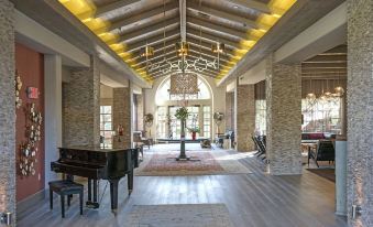 a large , open room with a high ceiling and wooden beams has a grand piano in the center at Bernardus Lodge & Spa