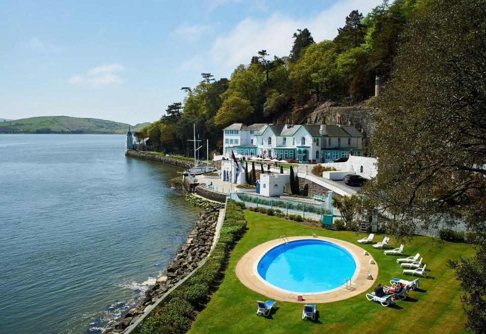 a beautiful coastal resort with a large swimming pool , surrounded by lush greenery and a calm sea at Portmeirion Village & Castell Deudraeth