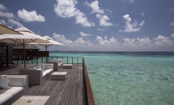 a wooden deck overlooking the ocean , with several lounge chairs and umbrellas placed around the area at Coco Bodu Hithi