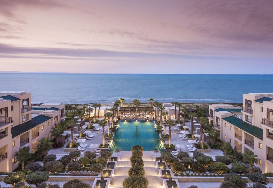 a luxurious resort with a large pool surrounded by palm trees , and a view of the ocean in the background at Four Seasons Hotel Tunis