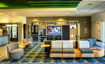 a modern hotel lobby with a green and blue patterned carpet , white furniture , and a television screen displaying a football game at Holiday Inn Richmond