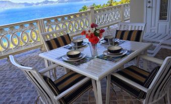 a white dining table set with plates , silverware , and a vase of flowers on a balcony overlooking the ocean at Ocean View Villas