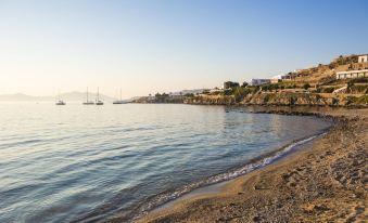 a serene beach scene with a sailboat floating in the water , surrounded by sand and rocks at Mykonos Beach Hotel