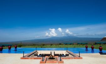 a large swimming pool with a mountain in the background and a person standing near the pool at Ngorongoro Oldeani Mountain Lodge