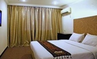 a well - lit hotel room with a large bed , white sheets , and gold curtains , along with an air conditioner on the wall at Royal Hotel
