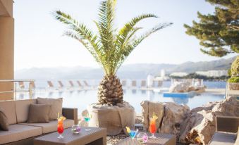 a tropical outdoor setting with a palm tree , lounge chairs , and an outdoor dining area near a pool at Hotel Dubrovnik Palace