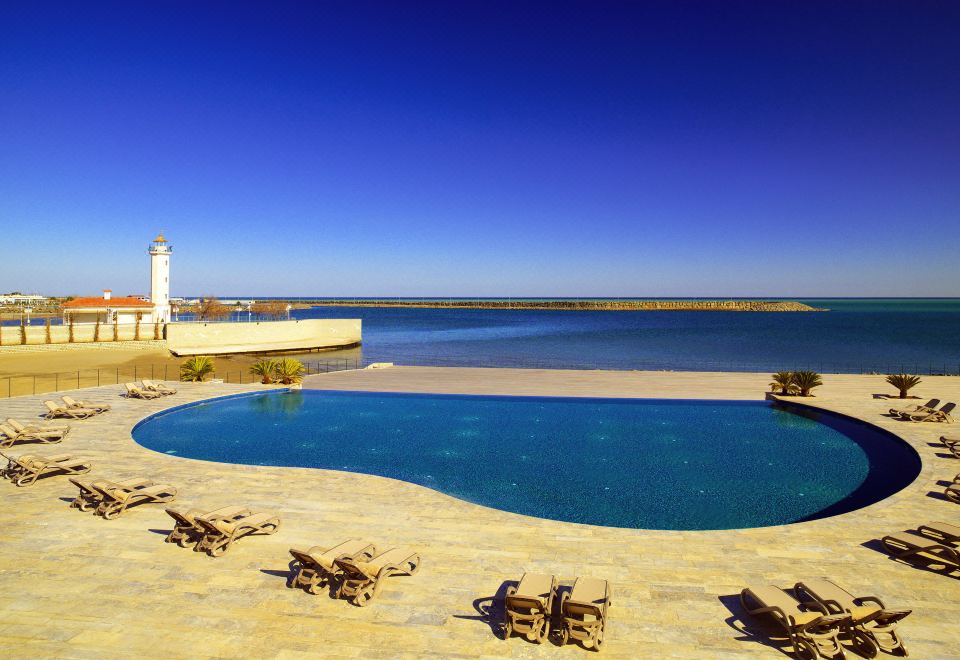 a beautiful pool and surrounding area with a lighthouse , including the iconic lighthouse on a pier , under a clear blue sky at Sheraton Grand Samsun Hotel