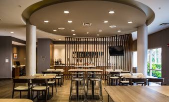 a modern restaurant with wooden tables and chairs , a bar , and a tv mounted on the wall at SpringHill Suites Vero Beach