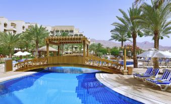 a beautiful resort with a blue swimming pool , sun loungers , and palm trees , surrounded by mountains in the background at InterContinental Hotels Aqaba (Resort Aqaba)