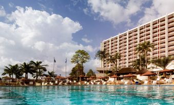a large swimming pool is in front of a tall hotel with palm trees and other buildings at Transcorp Hilton Abuja