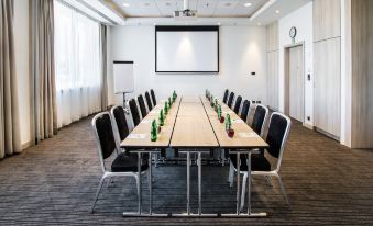 a long wooden table with chairs and green bottles is set up in a conference room at Park Inn by Radisson Krakow