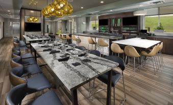 a modern dining area with a long table , several chairs , and a bar in the background at Holiday Inn & Suites Arden - Asheville Airport