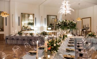 a long dining table is set with gold and white plates , glasses , candles , and flowers at The Dewberry Charleston