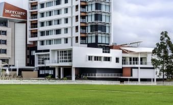 a tall white building with a green lawn in front of it , under a cloudy sky at Mercure Sydney Liverpool