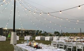 a well - decorated outdoor event with multiple tables set up under string lights , surrounded by white chairs at Club Tropical Resort Darwin