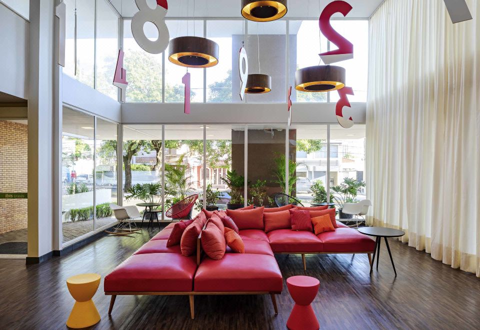 a modern living room with large windows , red couches , and hanging lights , creating a bright and modern atmosphere at Ibis Styles Piracicaba