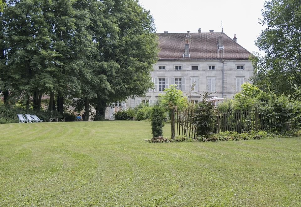 a large stone house surrounded by a lush green lawn , with a fence surrounding the property at Joie de Vivre