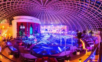 a large , circular room with a bar and pool area is illuminated by purple lights at Okada Manila