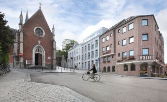 a man riding a bicycle down a city street , passing by a church and a brick building at Hotel the Shepherd