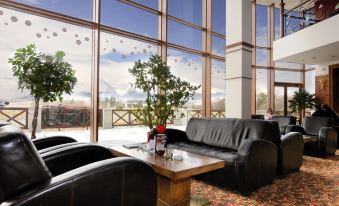 a living room with a large window and black leather couches , surrounded by windows that offer a view of the outdoors at Hotel International