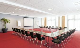 a large conference room with a long table , chairs , and a screen at the front at NH Vienna Airport Conference C