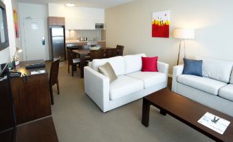 a modern living room with a white couch , wooden coffee table , and dining area in the background at Quest Mawson Lakes