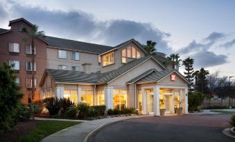 an exterior view of a hotel or motel , with a large building in the background at Hilton Garden Inn Gilroy