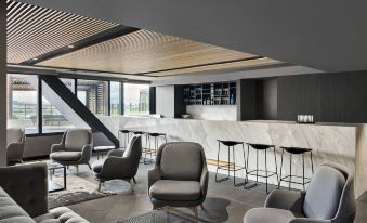 a modern bar with gray chairs and white marble counter , surrounded by a large glass window at Vibe Hotel Melbourne Docklands