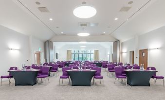 a large conference room with purple chairs arranged in rows and a chandelier hanging from the ceiling at Aubrey Park Hotel