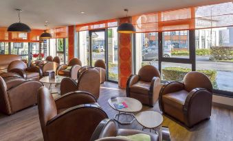 a modern and elegant lounge area with leather chairs and tables , large windows , and a view of an outside building at Ibis Styles Lille Marcq-en-Baroeul