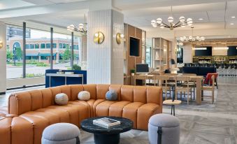 a modern lounge area with a large orange couch and black chairs , surrounded by tables and chandeliers at Delta Hotels Muskegon Convention Center