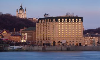 a large , modern hotel with a lit sign on top and the river in front of it at Fairmont Grand Hotel - Kyiv