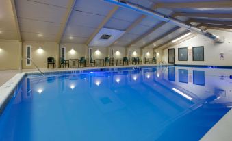 a large swimming pool with blue water and surrounding facilities , including tables and chairs , in a room with white walls at La Quinta Inn & Suites by Wyndham Springfield MA