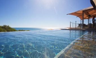 a large outdoor swimming pool surrounded by grass and trees , with a view of the ocean at Eco Beach Wilderness Retreat