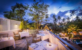 an outdoor dining area with a wooden deck , tables set for a meal , and lush greenery in the background at Malolo Island Resort