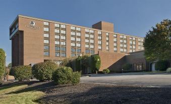 a large brick hotel with many windows and a sign on the front , surrounded by trees and bushes at DoubleTree Boston North Shore Danvers