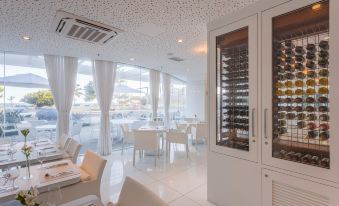 a modern restaurant with white tables and chairs , large windows , and a glass display case filled with wine bottles at CDesign Hotel