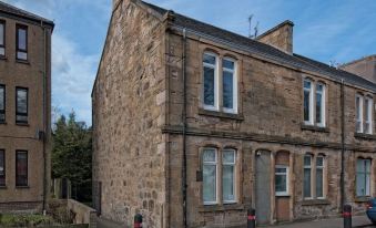 a stone building with a chimney , two windows , and a street corner in front of it at Carmel Apartments