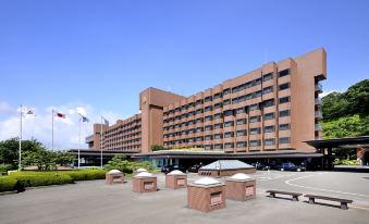 a large , modern building with a red brick facade and many windows , surrounded by parking spaces and umbrellas at SHIROYAMA HOTEL kagoshima