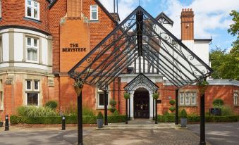 a brick building with a glass roof and a metal roof , surrounded by trees and grass at Macdonald Berystede Hotel & Spa