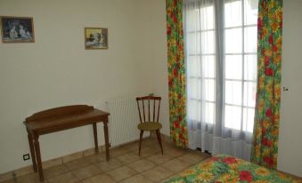 a room with a wooden desk , a chair , and a window with colorful curtains , as well as a painting on the wall at L'Horizon