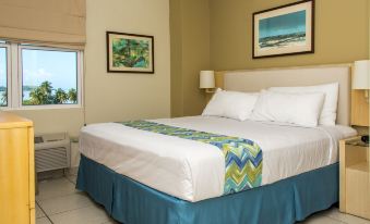 a large bed with a blue skirt and white sheets is in a room with two paintings on the wall at Aquarius Vacation Club at Boqueron Beach Resort
