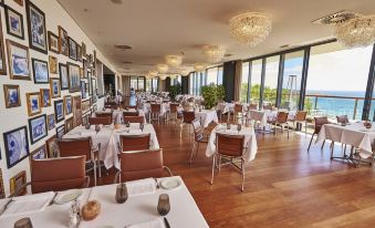 a large , empty dining room with wooden floors and high ceilings , decorated with white tablecloths and chairs at Martinhal Sagres Beach Family Resort Hotel